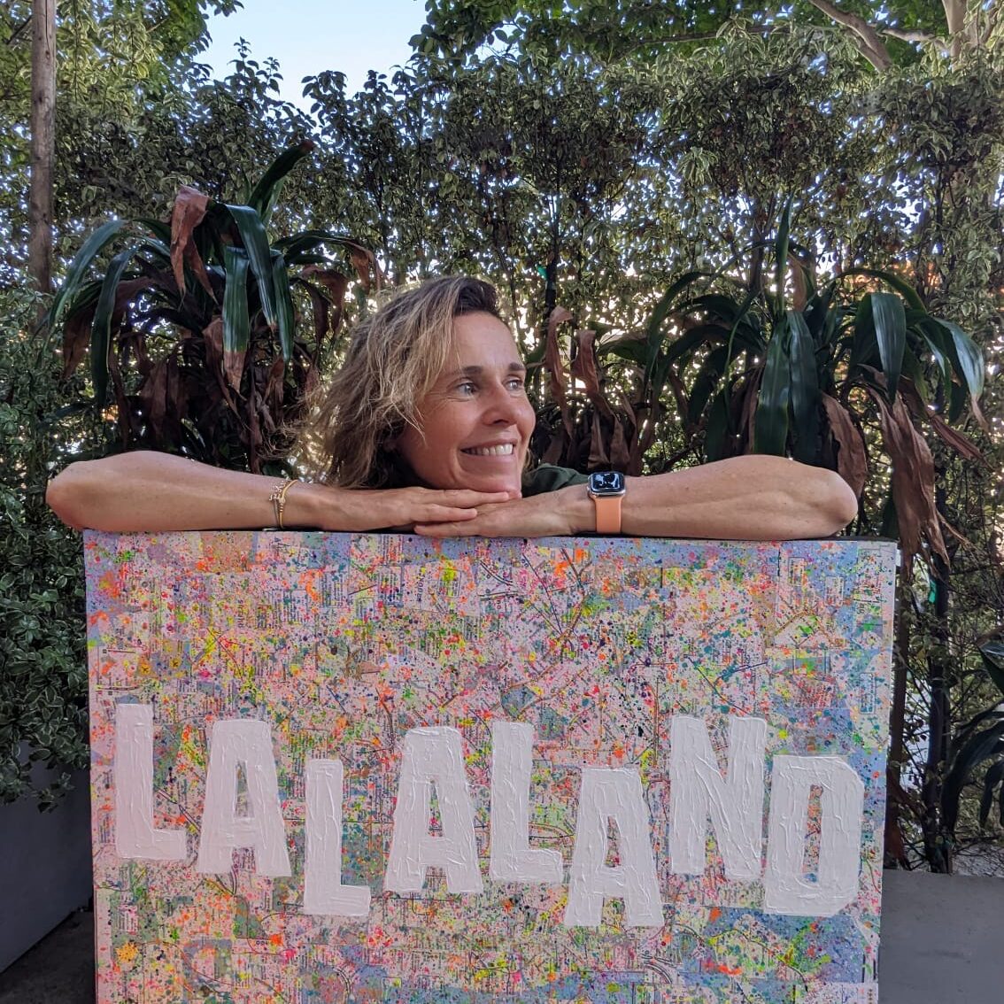 Artist, Adele French, holding a piece of art with the words "Lala Land" on canvas.