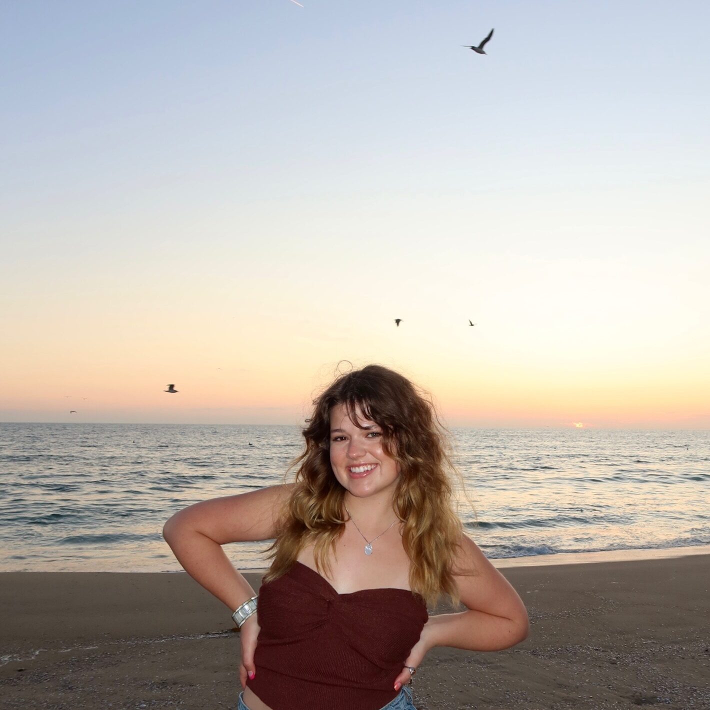 Photo of Sam Homan on the beach with her arms on her hips.